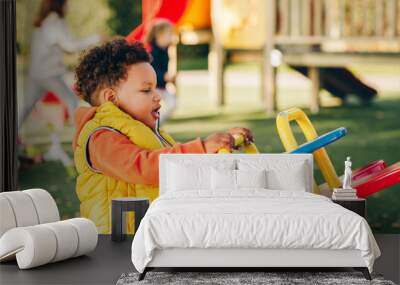 Adorable little 1-2 year old toddler boy having fun on playground, child wearing orange hoody jacket and yellow vest Wall mural