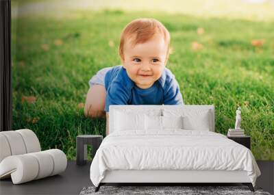 Adorable red haired baby boy crawling on fresh green grass in summer park Wall mural