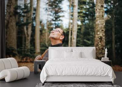 Handsome middle age man hiking in forest, wearing pullover, backpack and glasses Wall mural