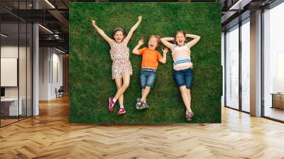 Happy children having fun outdoors. Kids playing in summer park. Little boy and two girls lying on green fresh grass Wall mural