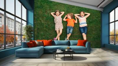 Happy children having fun outdoors. Kids playing in summer park. Little boy and two girls lying on green fresh grass Wall mural