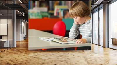 Little preschooler boy of 5 years old reading book in the library Wall mural