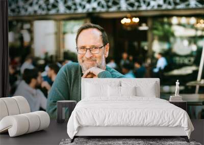 Outdoor portrait of 50 - 55 year old man wearing green pullover and eyeglasses, arms crossed Wall mural