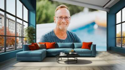 Outdoor portrait of 50 year old man resty by the pool, wearing blue t-shirt and glasses Wall mural