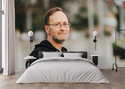 Outdoor portrait of 50 year old man wearing black hoody and eyeglasses Wall mural