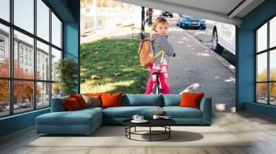 Outdoor portrait of a cute little toddler girl, riding a bike, wearing backpack Wall mural