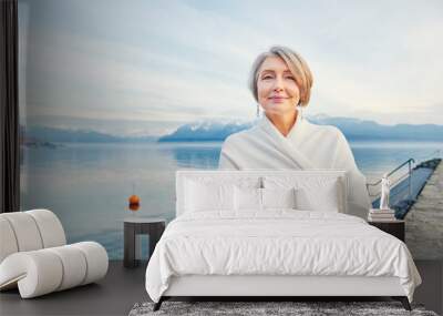 Outdoor portrait of beautiful middle age woman posing next to winter lake, wearing white coat Wall mural