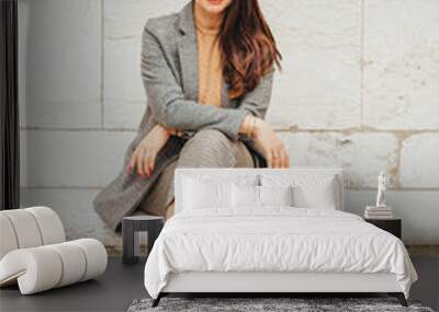 Outdoor portrait of beautiful woman resting in park, sitting on bench, wearing checked trousers and coat Wall mural