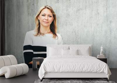 Outdoor portrait of middle age woman, leaning on grey wall Wall mural