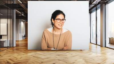 Studio portrait of beautiful brunette woman, wearing glasses, arms crossed, posing on white background Wall mural