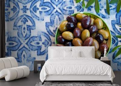 Assortment of fresh olives on a plate with olive tree brunches. Blue textile background. Copy space. Top view. Wall mural