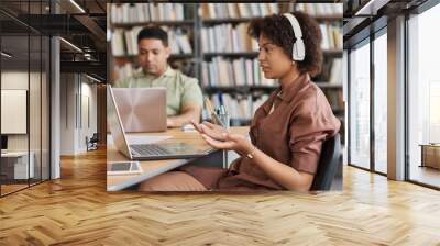 African American student in wireless headphones studying foreign language online while sitting at table with computer Wall mural