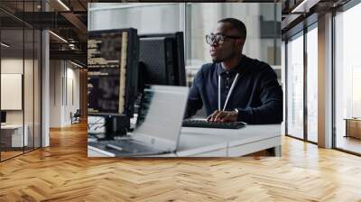 african american young developer in eyeglasses concentrating on his online work on computer sitting  Wall mural