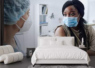 African woman in mask discussing consequences of vaccine together with doctor at hospital Wall mural