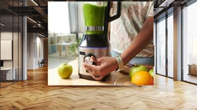 Close-up of young girl turning on the button on blender to make green vitamin smoothie at table while she on a diet Wall mural