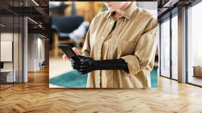 Close-up of young woman in shirt with prosthetic arm learning to use her smartphone Wall mural