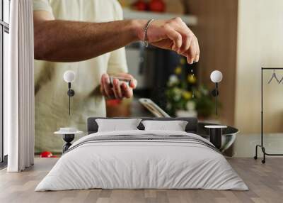 Closeup of hands of unrecognizable man adding salt to meal in pan on kitchen stove Wall mural