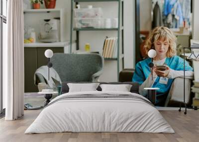 Focused Caucasian nurse resting on black sofa in on call room while texting with her patient on social media Wall mural