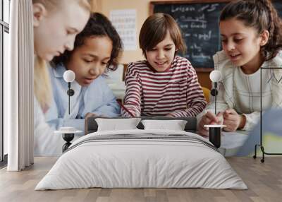 Group of ethnically diverse kids sitting at table in classroom doing exercise together during English lesson Wall mural