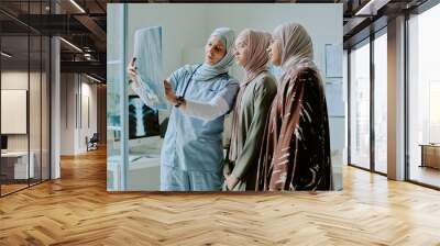 Healthcare professional showing medical scan to two women wearing hijabs in modern clinic setting creating a collaborative and informative atmosphere Wall mural