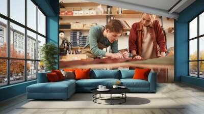 Horizontal shot of two young concentrated man and woman working together in modern leather craft workshop Wall mural