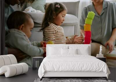 Little Asian girl playing with multicolored bricks while her mother and African American aunt helping her, baby boy playing with rattle in mothers arms Wall mural