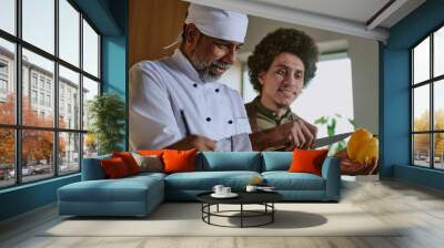 Low angle shot of Indian professional chef showing peeling skills to his intern Wall mural