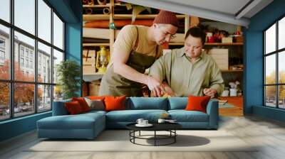 Male tailor helping his female coworker with down syndrome to cut out leather detail while they working in atelier together Wall mural