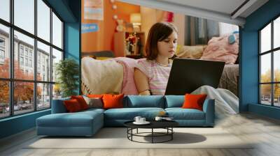 Modern teen girl with disability sitting on floor against her bed and watching educational video on laptop, copy space Wall mural