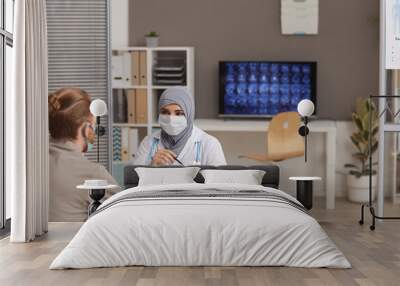 Muslim female doctor in protective mask prescribing the medicine to the male patient while they sitting at hospital Wall mural