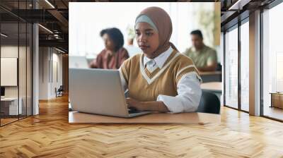 Muslim girl sitting at desk and using laptop during lesson in classroom Wall mural