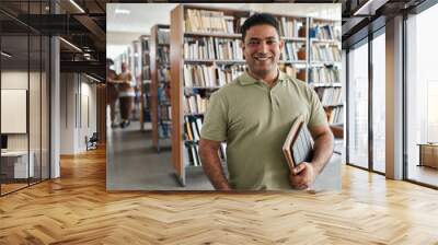 Portrait of adult student smiling at camera while standing in the library Wall mural