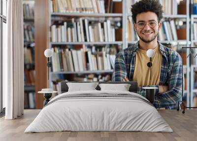 Portrait of adult student standing with his arms crossed and smiling at camera in library at college Wall mural