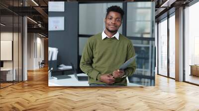 Portrait of African American businessman looking at camera standing in modern office with his workplace in background Wall mural