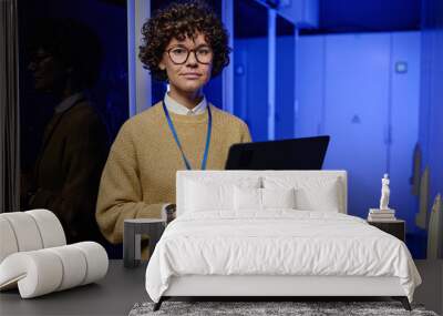 Portrait of female technician in eyeglasses using her laptop while working in data center with computer system Wall mural