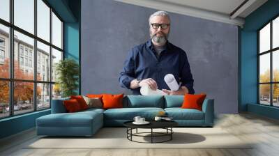 Portrait of mature bearded architect in eyeglasses standing with blueprints against the black background Wall mural