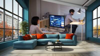 Rear view of young businesswoman sitting at her workplace and working online with financial report with businessman working at the table in the background Wall mural