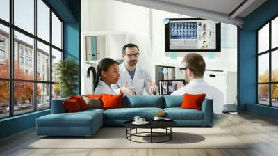 Team of doctors sitting at the table and discussing x-ray images together during online conference with their colleagues Wall mural