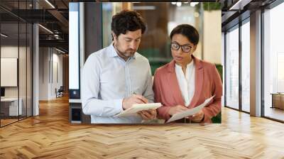 Two business colleagues checking their notes and comparing the business plan while standing at office Wall mural