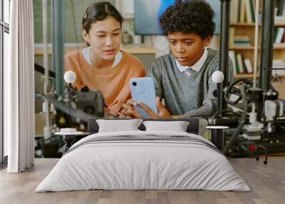 Two students observing a 3D printer's progress in a classroom setting involving technology education. Close-up view of their focused expressions showing concentration around printer setup equipment Wall mural