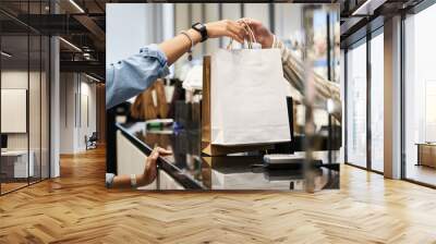 Unrecognizable cashier giving paper bags with purchases to unknown customer at clothing store Wall mural