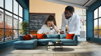 Young African American teacher of Chemistry wearing lab coat giving microscope slide to Middle Eastern student, copy space Wall mural