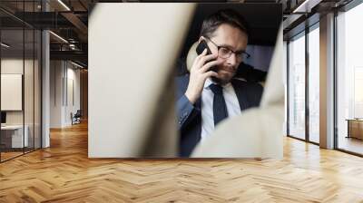 Young bearded businessman in eyeglasses sitting on back seat of the car and talking on mobile phone Wall mural