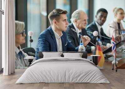 Young businessman sitting at the table and speaking the speech during debates with other political leaders Wall mural