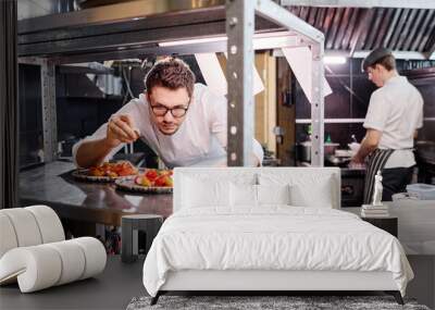 Young cookin eyeglasses decorating vegetable salad on plate with herbs on the counter before serving Wall mural