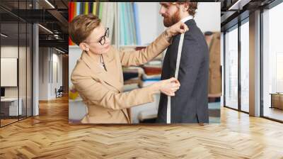 Young fashion designer measuring the sleeve of jacket with tape measure while working with her client Wall mural