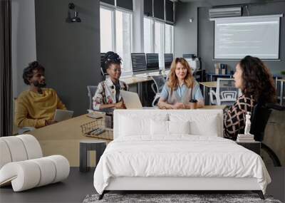 Young female office worker in wheelchair talking to colleagues sitting at desk at business meeting Wall mural