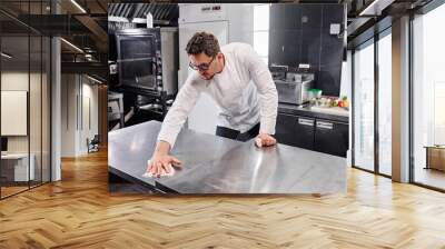 Young professional cook in uniform wiping kitchen counter in kitchen after cooking Wall mural