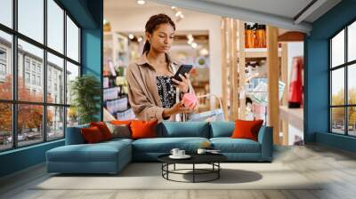 Young woman making photo of cream on her smartphone during shopping in cosmetics store Wall mural