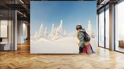 Female snowboarder wearing long dreadlocks and hoody holding a board, walking in snow-covered winter forest. Sheregesh, Siberia Wall mural